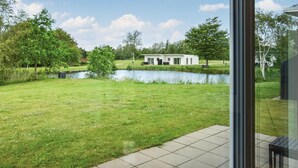 Uma casa moderna com um lago, rodeada por vegetação e árvores.