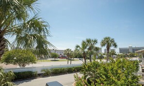 A parking lot with a vehicle, surrounded by palm trees and a white fence.
