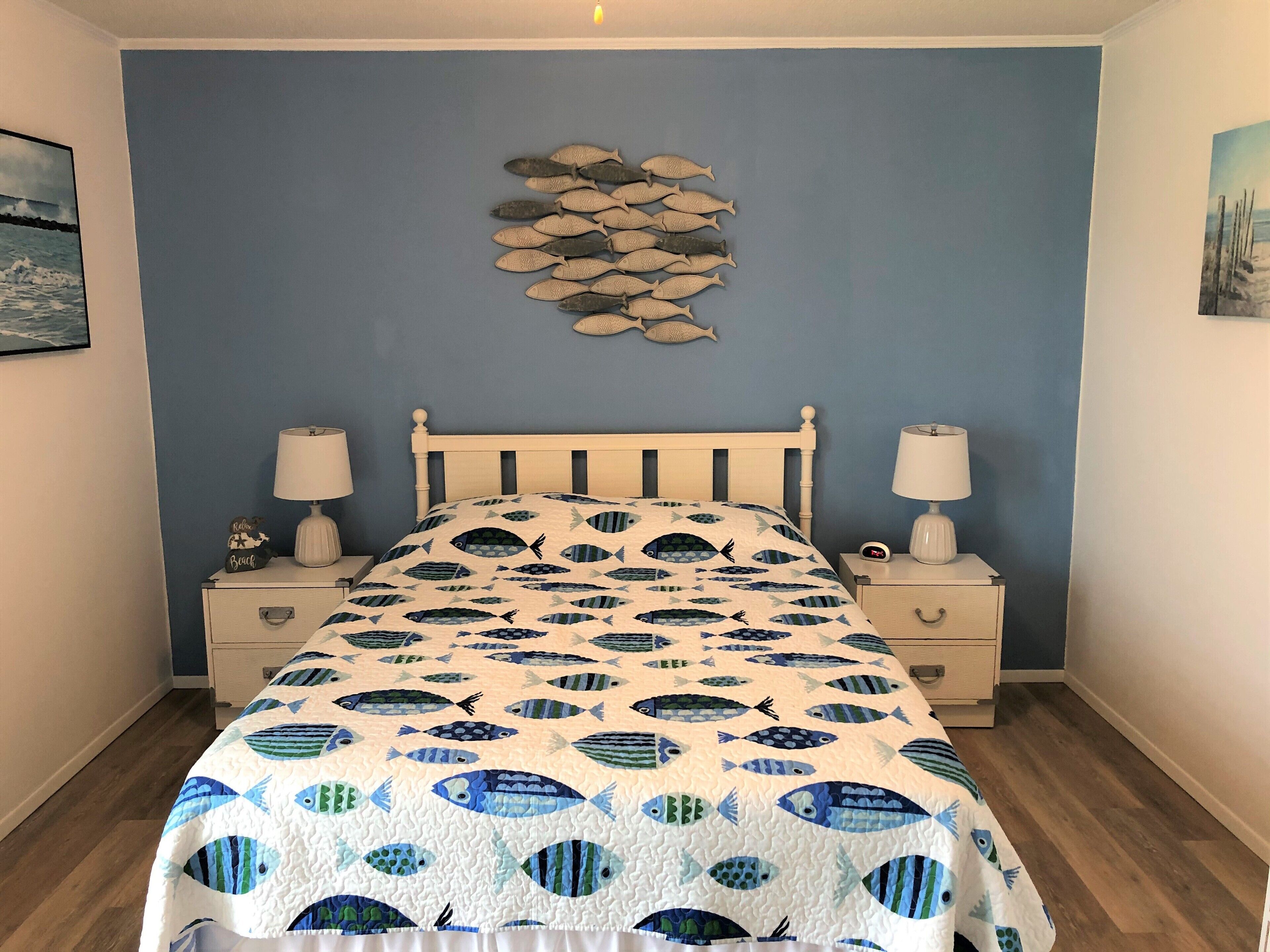 Un dormitorio con cama, mesitas de noche y un adorno de peces en la pared.
