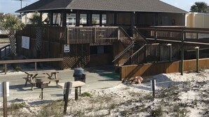 Een gebouw aan het strand met een overdekt terras, een houten dek en een bord voor strandverhuur.