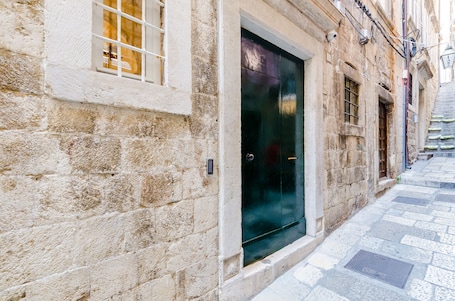 A stone building with a dark door, a window with bars, and a narrow street.