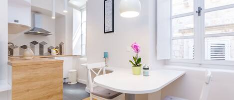 A modern kitchen with a white table, chairs, and a potted plant.