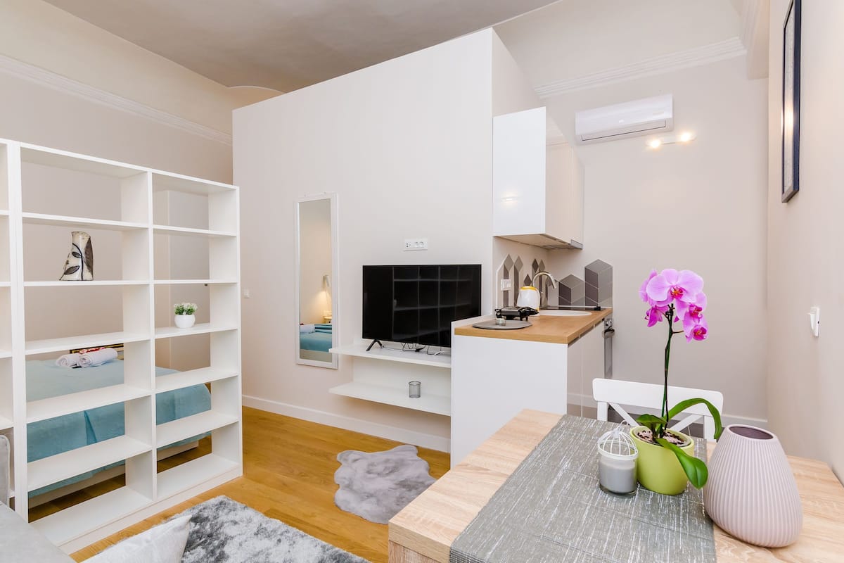 Ein modernes Wohnzimmer mit Fernseher, weißen Regalen, einem kleinen Tisch mit Dekoration und Holzboden.