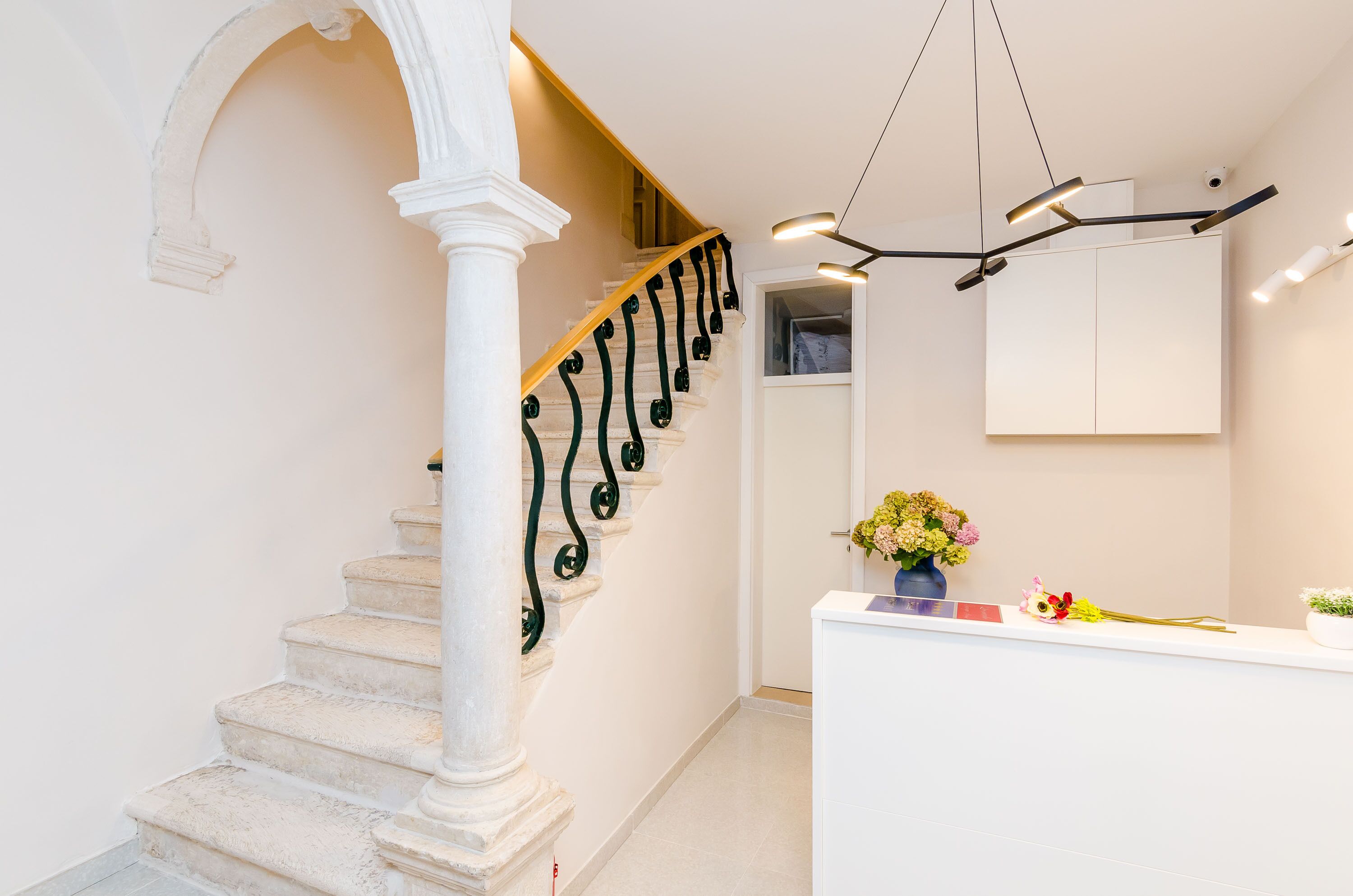 A staircase with white steps and black balusters, leading to a reception area with a white desk and a vase of flowers.