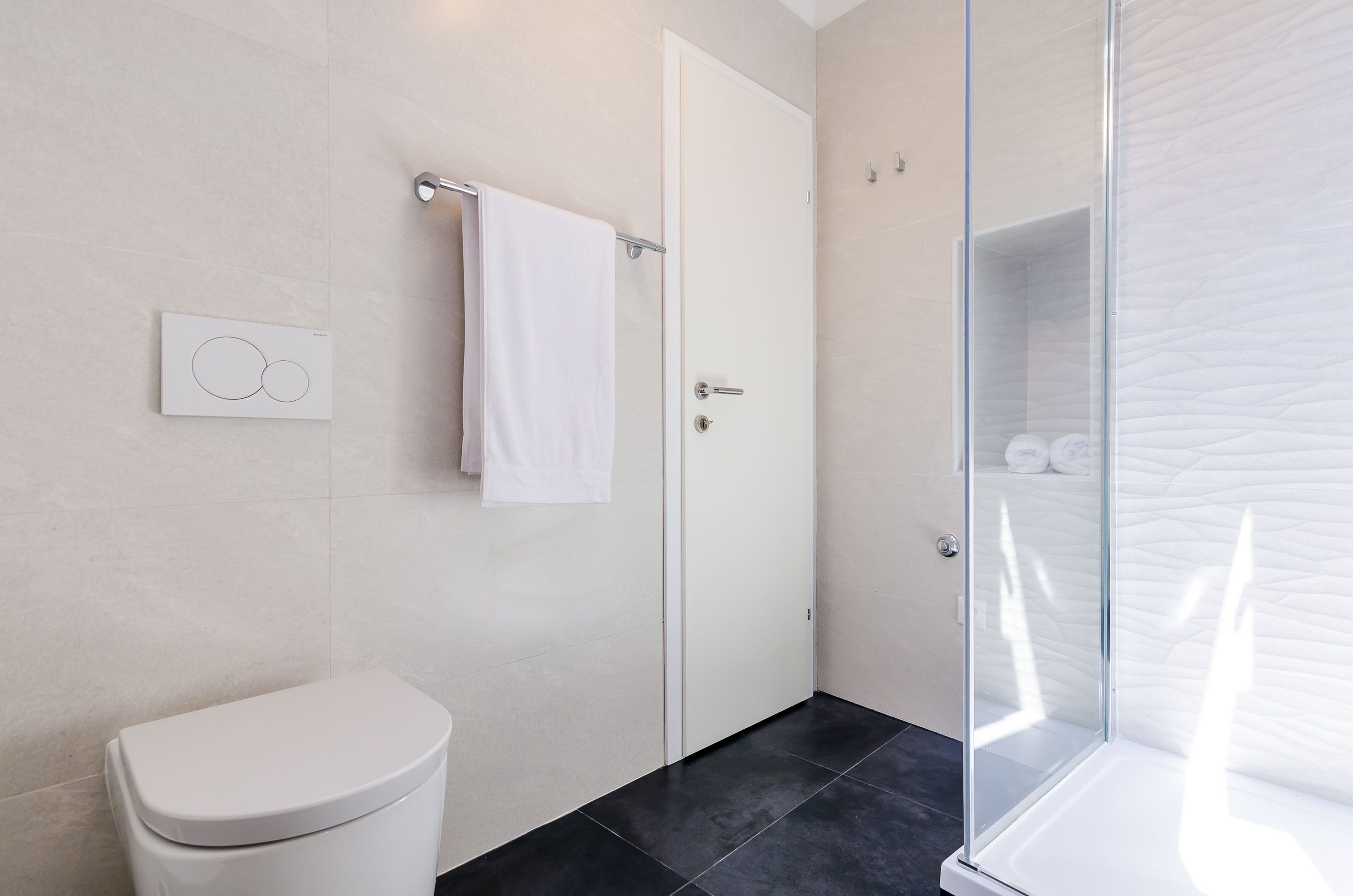 A modern bathroom with a toilet, a towel rack, a glass shower enclosure, and a wall-mounted control panel.