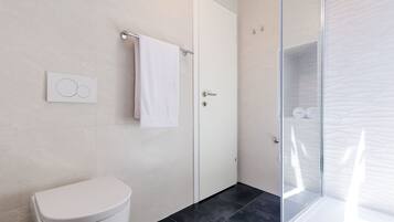 A modern bathroom with a toilet, a towel rack, a glass shower enclosure, and a wall-mounted control panel.