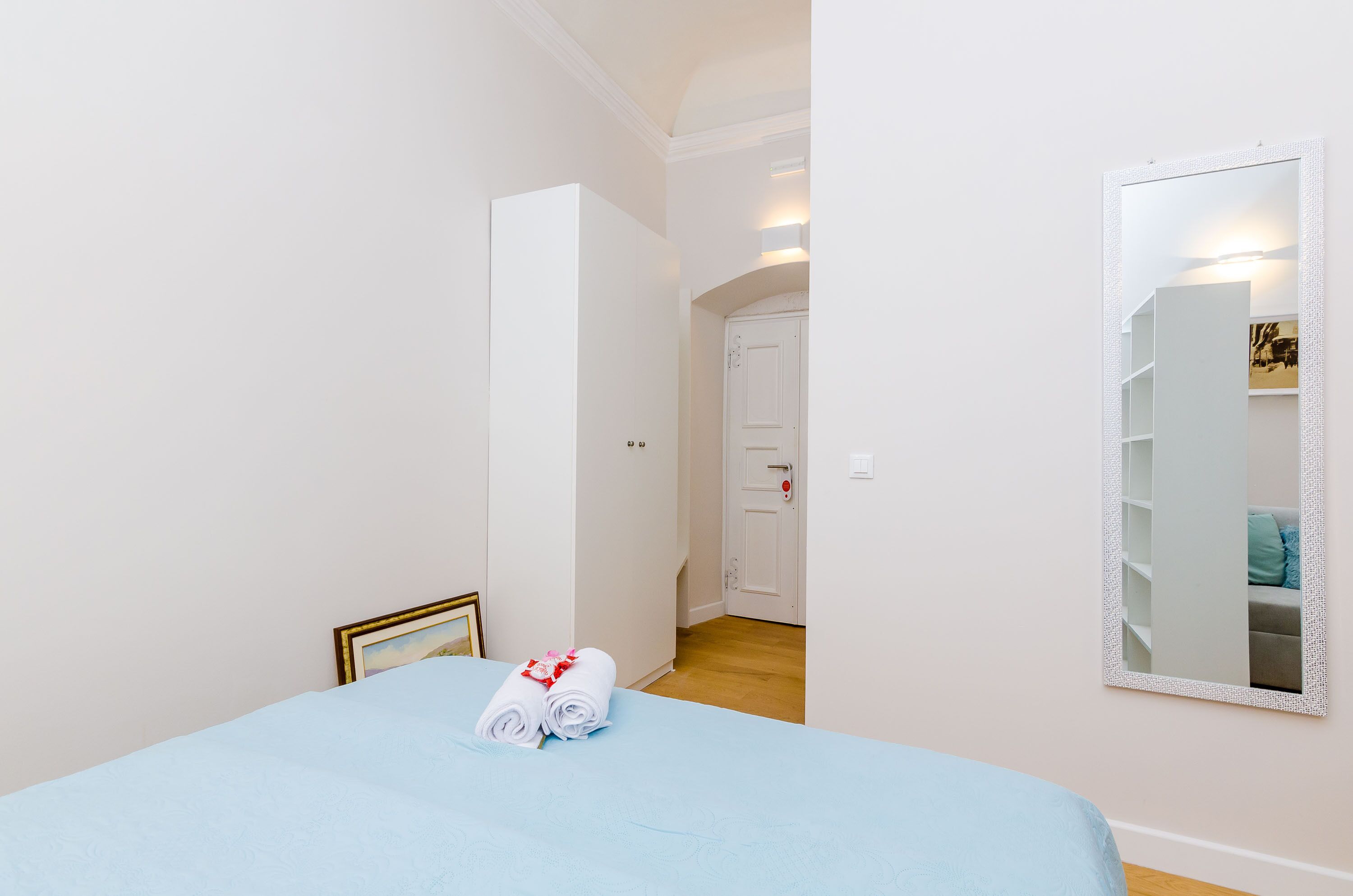 A hotel room with a bed, a door, and a mirror on the wall.