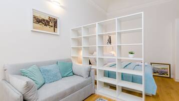 A modern living room with a grey sofa, teal cushions, a white shelving unit, and a framed picture on the wall.