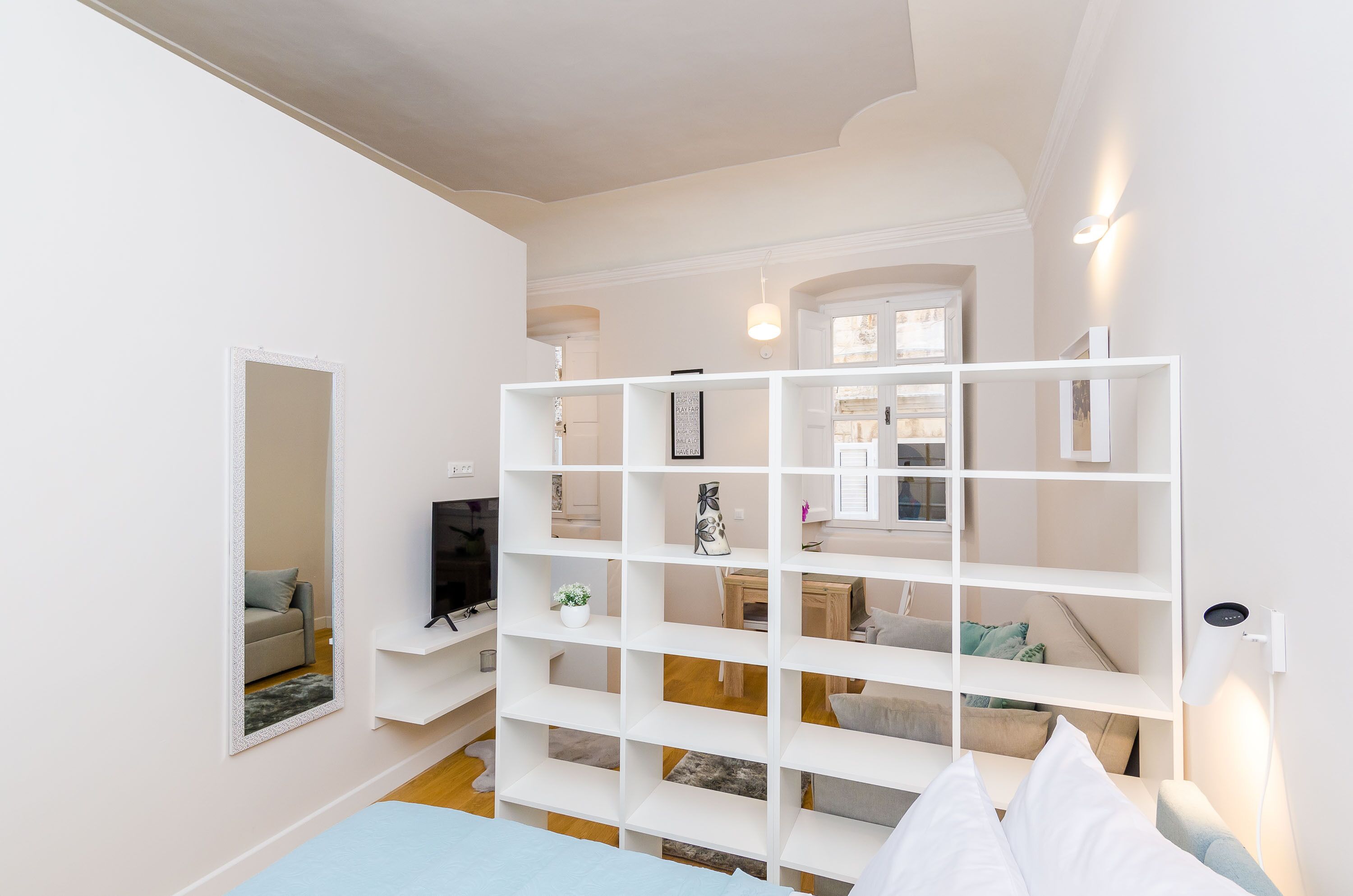 Una stanza moderna e luminosa, con un'ampia libreria bianca, una TV a schermo piatto e un'accogliente area salotto con cuscini.