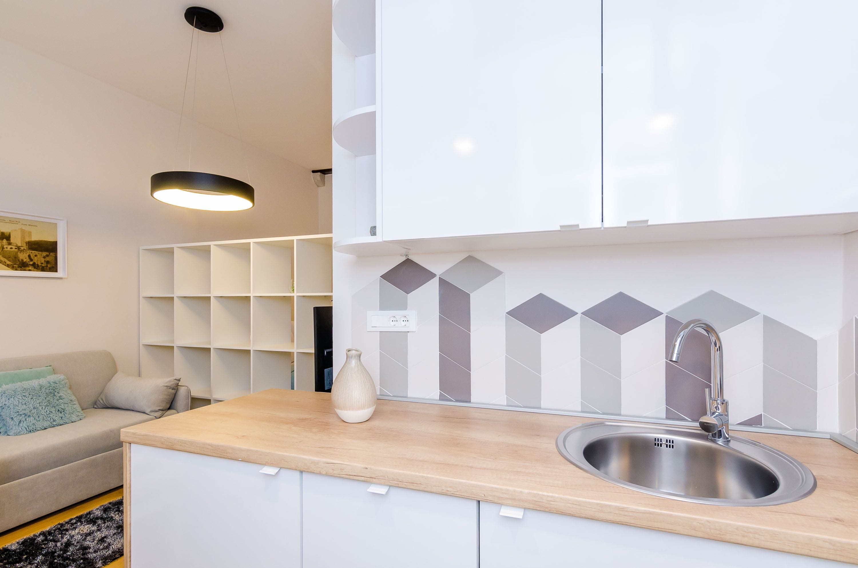 A modern kitchen with a stainless steel sink, white cabinets, and a geometric backsplash.