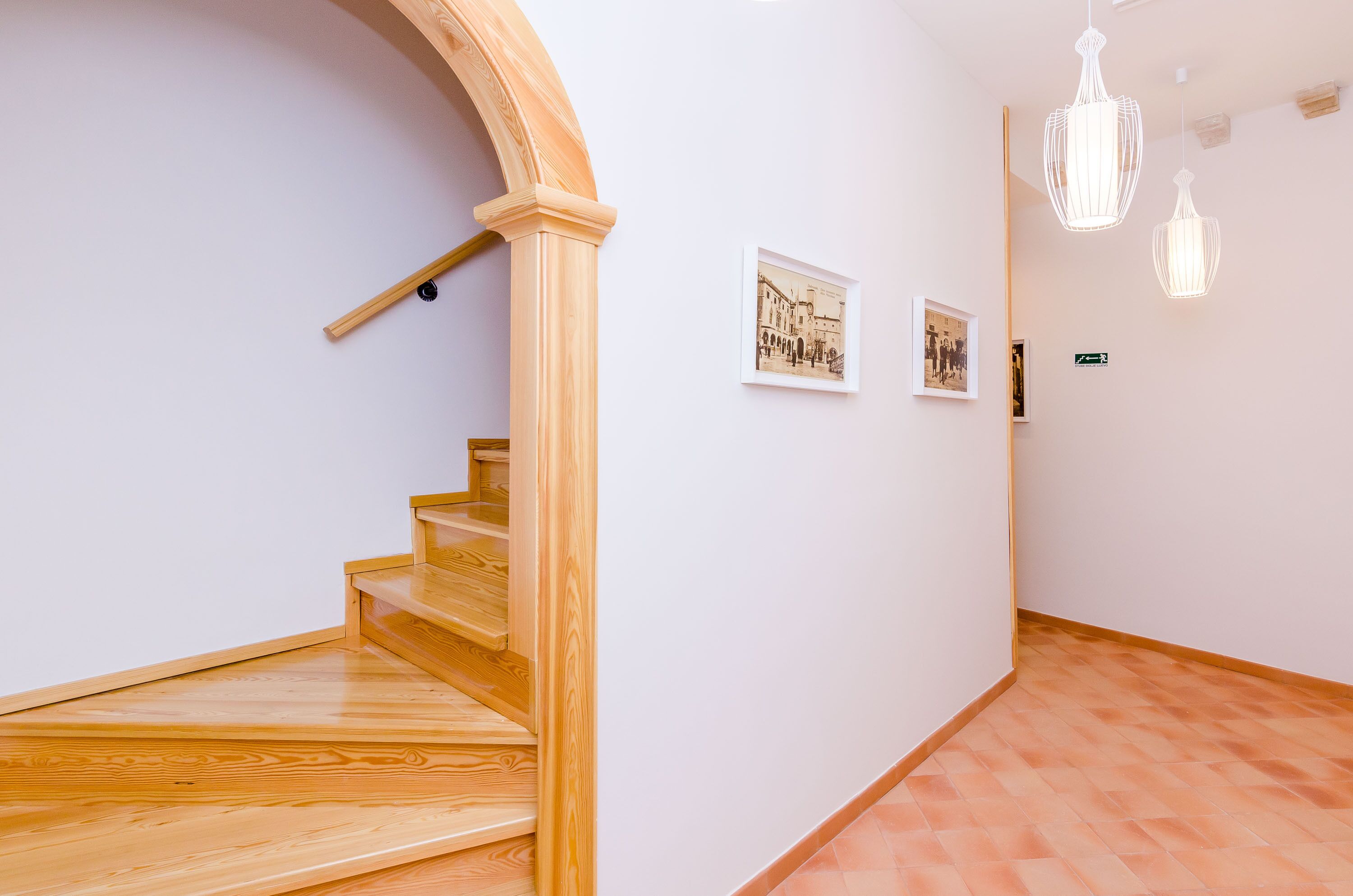 Een trap met houten treden en een houten leuning, die leidt naar een plateau met een witte muur en twee ingelijste foto's.