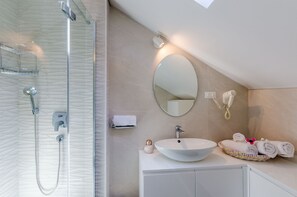 Une salle de bain moderne avec une douche à parois de verre, un miroir rond, un lavabo et des serviettes soigneusement rangées.
