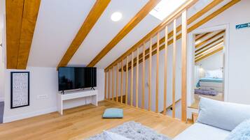 Camera da letto moderna in stile loft con travi in legno, TV, letto e una scala che conduce a un'altra stanza.