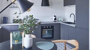 A modern kitchen with grey cabinets, a black pendant light, a round table with chairs, and a potted plant. - Metro Politechnika Studio (Warsaw)
