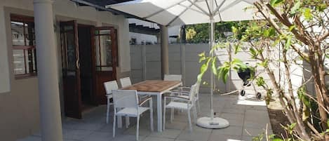A patio with a table and chairs, a white umbrella, and a potted plant.