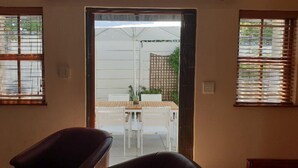 Une pièce avec une porte donnant sur un espace extérieur, une table avec des chaises et une fenêtre avec des stores.