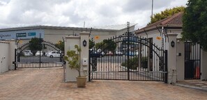 A gated entrance with a paved driveway leading to a building with a modern design. - High Grove Cottage (Cape Town)