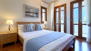 A neatly arranged bedroom with a large bed, two bedside tables with lamps, a framed picture on the wall, and a view through the glass doors. - Apartment DD12 - Chloe (Kouklia)