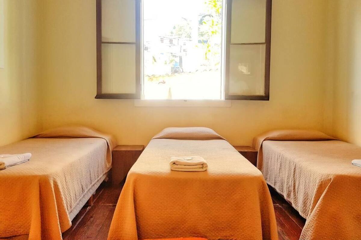 Quarto com duas camas, janela com persianas abertas e vista para o exterior.