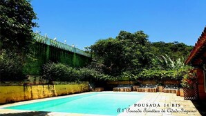 A swimming pool with a green bridge and lush greenery. - Pousada 14 Bis (Petrópolis)