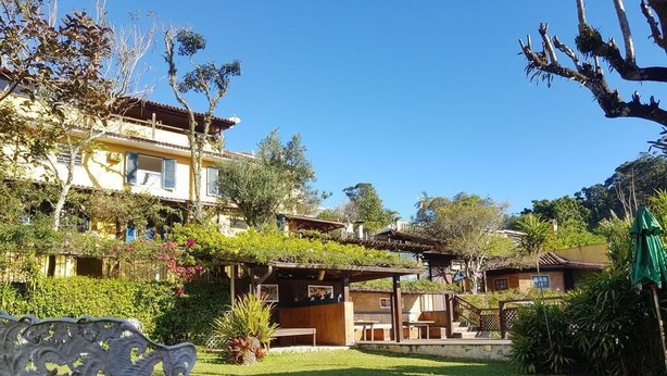 A courtyard with a bench, a pergola, and a building with multiple levels and balconies. - Pousada 14 Bis (Petrópolis)