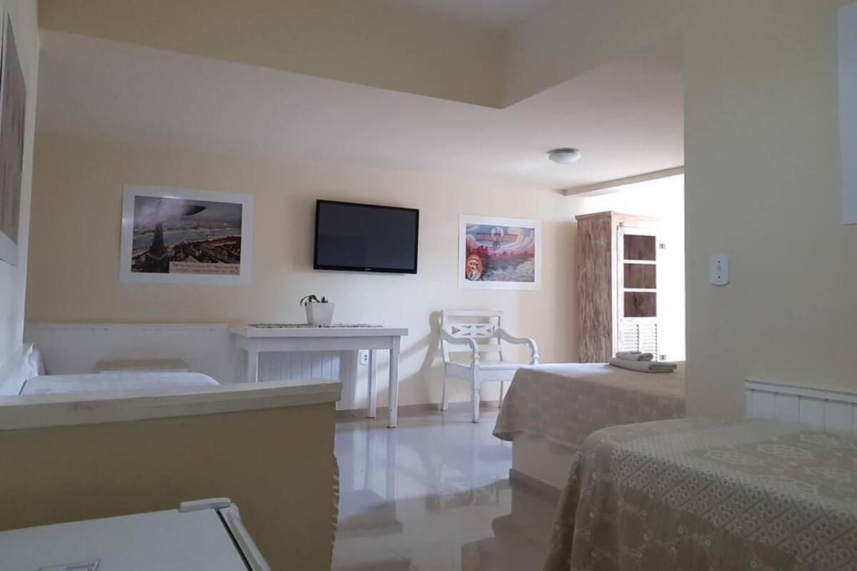 Quarto de hotel com cama, mesa de trabalho, cadeira e televisão na parede.