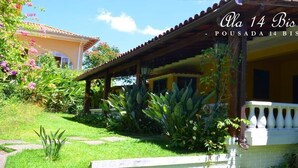 A covered outdoor area with a tiled roof, surrounded by lush greenery and flowering plants. - Pousada 14 Bis (Petrópolis)