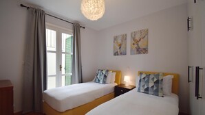 Un dormitorio con dos camas, un aparador, una mesita de noche con lámpara y una obra de arte en la pared.