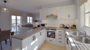 Una cocina moderna con armarios blancos, encimera de granito, electrodomésticos de acero inoxidable y un amplio ventanal que proporciona luz natural.