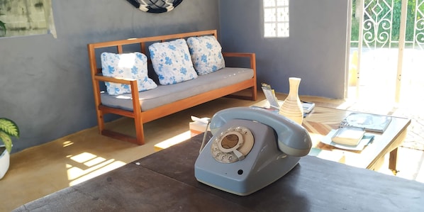 A room with a wooden sofa, a vintage telephone, and a table with books and a vase.