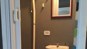 A small bathroom with a toilet, a sink, a mirror, and a shower. - Guapuruvu Suítes & Camping (Paraty)