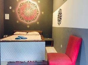 A bedroom with a bed, a red chair, and decorative wall art.
