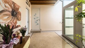 Un pasillo con techo de madera, una puerta decorada con motivos florales y plantas en macetas.