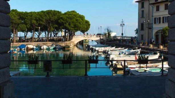 Un arco enmarca un puerto deportivo con barcos, árboles y edificios.