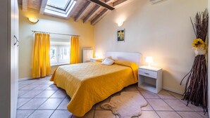 Un dormitorio con cama, mesitas de noche, ventana con cortinas y tragaluz.