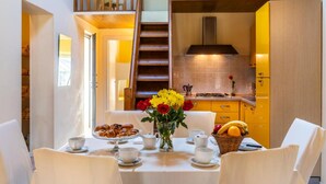 Un comedor con una mesa lista para el desayuno, una cocina al fondo y una escalera que sube a un nivel superior.