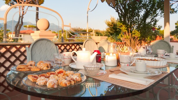 A table set for a meal with pastries, a teapot, cups, and a candle. - Forte Inn (Forte dei Marmi)