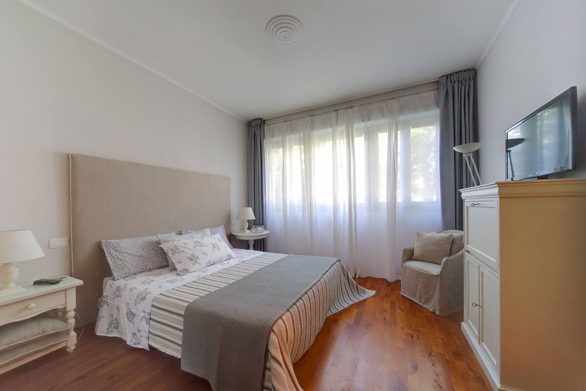 Ein Schlafzimmer mit Bett, Nachttisch, Lampe, Fernseher und Kleiderschrank.