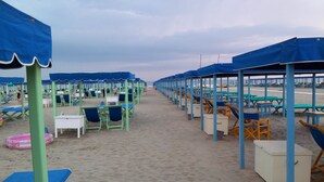 A beach with rows of blue and white beach chairs and tables under blue umbrellas, arranged on sandy ground. - Forte Inn (Forte dei Marmi)