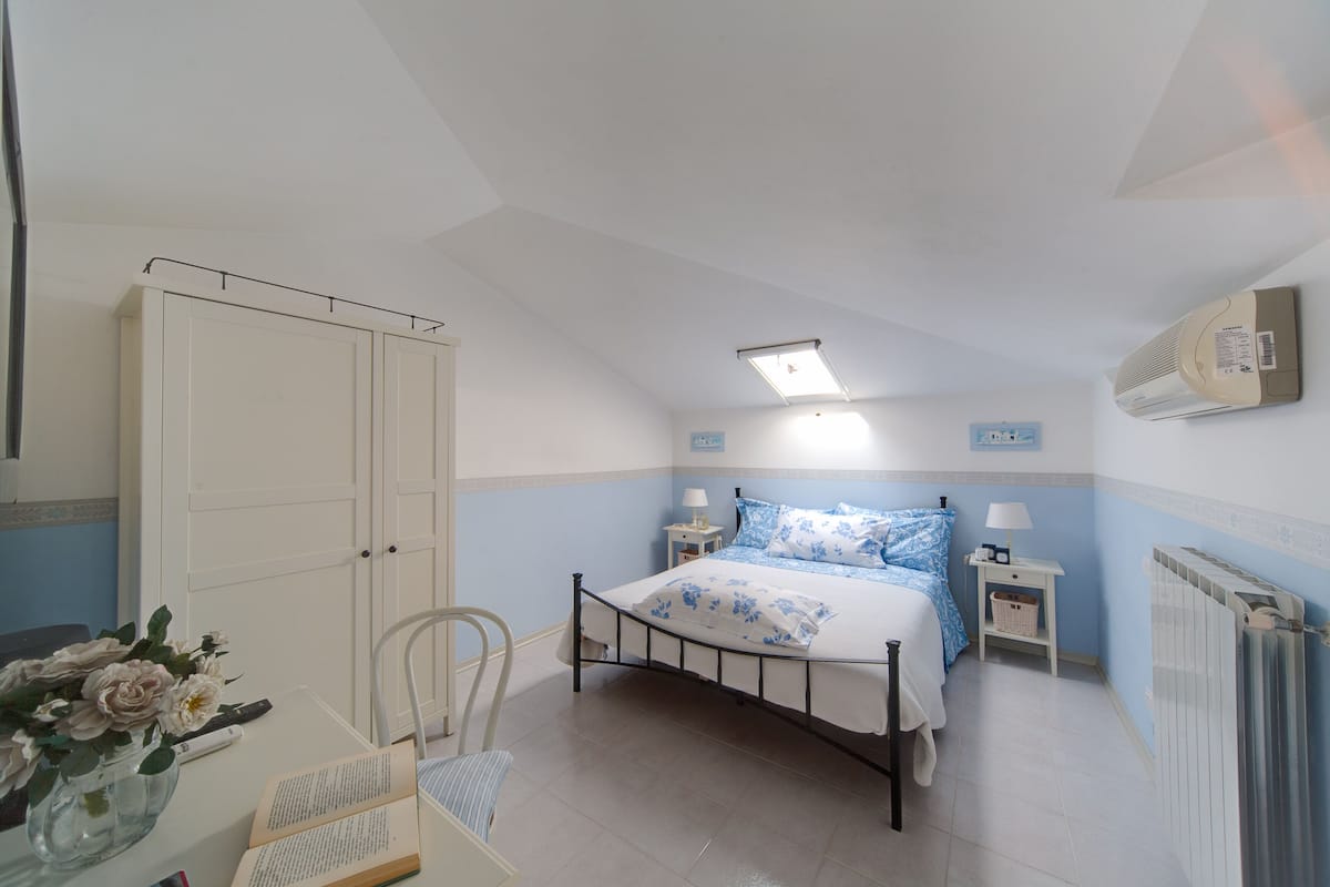 Ein Schlafzimmer mit Bett, Nachttischen, einem Sessel, einem Schreibtisch, einem Heizkörper und einem Kleiderschrank.