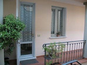 Ein Gebäudeeingang mit Glastür, einem Blumentopf links und einem Fenster mit einem Blumentopf rechts.