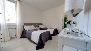 A bedroom with two beds, a bedside table, a mirror, and a window with curtains. - Forte Inn (Forte dei Marmi)