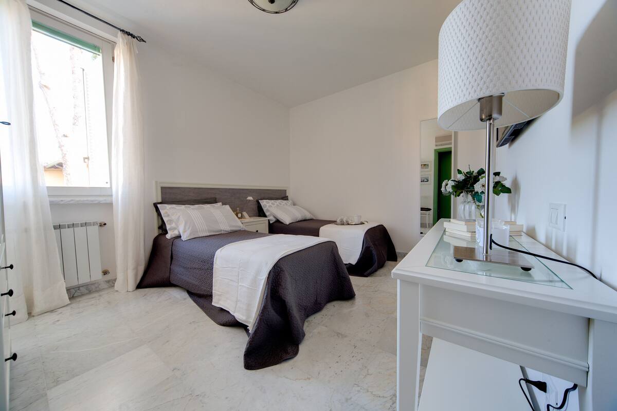 Ein Schlafzimmer mit zwei Betten, einem Nachttisch, einem Spiegel und einem Fenster mit Vorhängen.