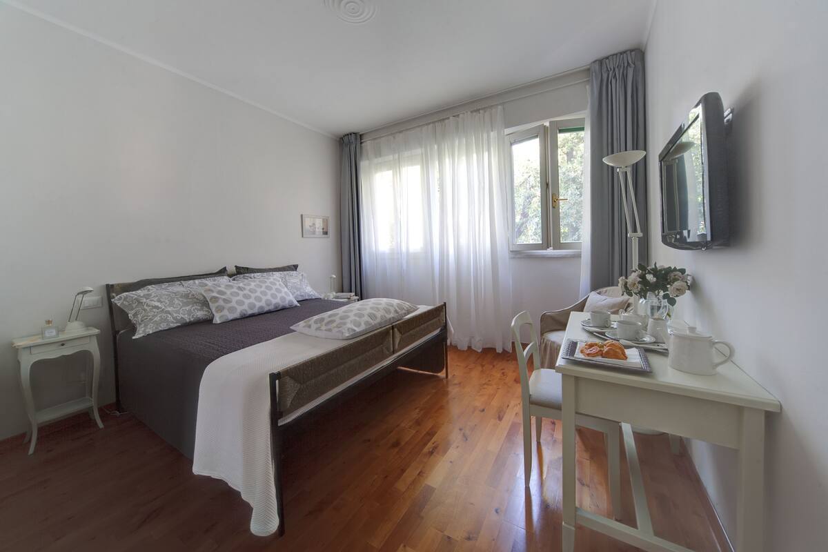 Ein Schlafzimmer mit Bett, Nachttisch, Stuhl, Schreibtisch und einem Fenster mit Vorhängen.