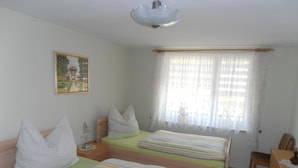 A room with two beds, a wooden dresser, a desk, a chair, a nightstand, a lamp, and a painting on the wall.