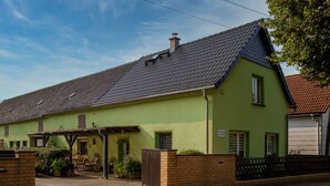 A green house with a tiled roof, a covered patio, and a brick entrance.