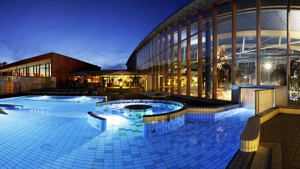 A swimming pool with a hot tub, lounge area, and a building with large windows.