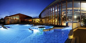 Una piscina con hidromasaje, zona de descanso y un edificio con ventanales amplios.