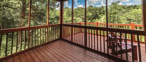 A wooden deck with a railing overlooking a forested area.