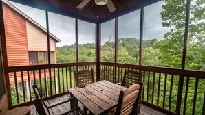 A wooden deck with a table and chairs, overlooking a forested area. - Cabins at Grand Mountain (Branson)